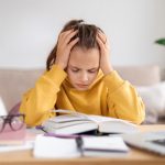 enfant se prenant la tête devant des cahier et des devoirs